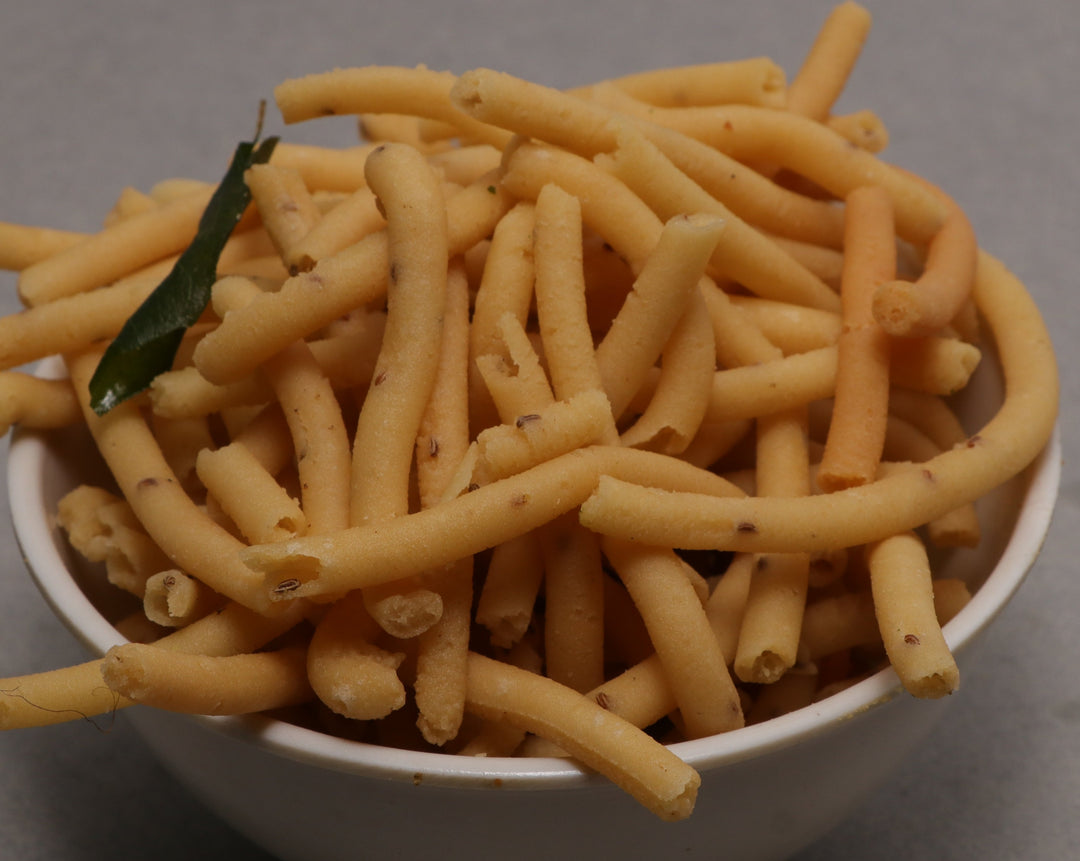 A bowl of Garlic Murukku, which are crispy fried snacks with a creamy pungent flavor, garnished with a green leaf on top.