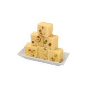 Stack of square-shaped Ghee Soan papdi on a white plate, garnished with nuts.