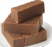 A stack of brown, rectangular karupatti Mysorepak snack cakes on a white plate.