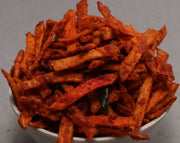A bowl of fried potato chips with a red savory masala coating, placed on a grey surface.