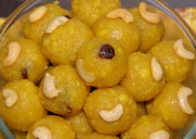 A clear glass bowl filled with freshly made laddu, a traditional Indian sweet, with visible nuts and spices.