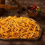 A plate of golden-brown Kuthiraivali Sattur Karasev, which are crispy snacks, placed on a wooden surface with a bowl of spices in the background.