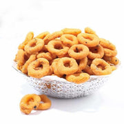 A silver bowl filled with Andhra Round Murukku snacks, with a few extra snacks scattered outside the bowl.