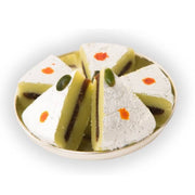 A plate of kaju anjeer sandwich sweets, which are triangular in shape with a visible cashew layer and a fig filling, garnished with a drop of rose water on top.