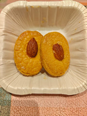 Two badam biscuits on a disposable paper plate, with almonds placed on top of each biscuit.