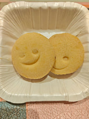 Two cookies with smiling face designs on a white plate.
