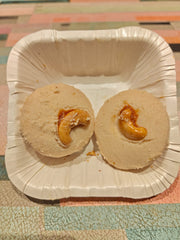 Two cashew vanilla cookies on a white disposable plate, with one cookie cut in half to show the cashew filling.