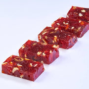 Sliced pomegranate halwa with visible nuts, on a white background.