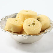 A silver bowl containing several round milk pedas, which are traditional Indian sweets made from milk and sugar, garnished with nuts on top.