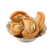 A silver bowl containing freshly fried Chandrakala sweets, which have a crispy outer layer and are soaked in a sugar syrup with cardamom and saffron.