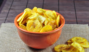 Bowl of yellow plantain chips on a wooden surface